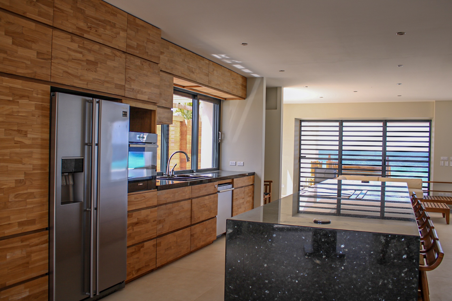 Luxury Bonaire villa gourmet kitchen with custom teak wood cabinets, black granite island, stainless steel appliances, and open-plan view of the Caribbean ocean.